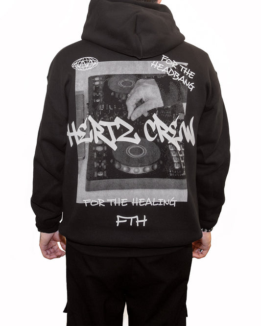 Person wearing a black hooded sweatshirt with a halftone print of dj decks being played. Includes hertz crew in graffiti font, handwritten text and logo on the back.