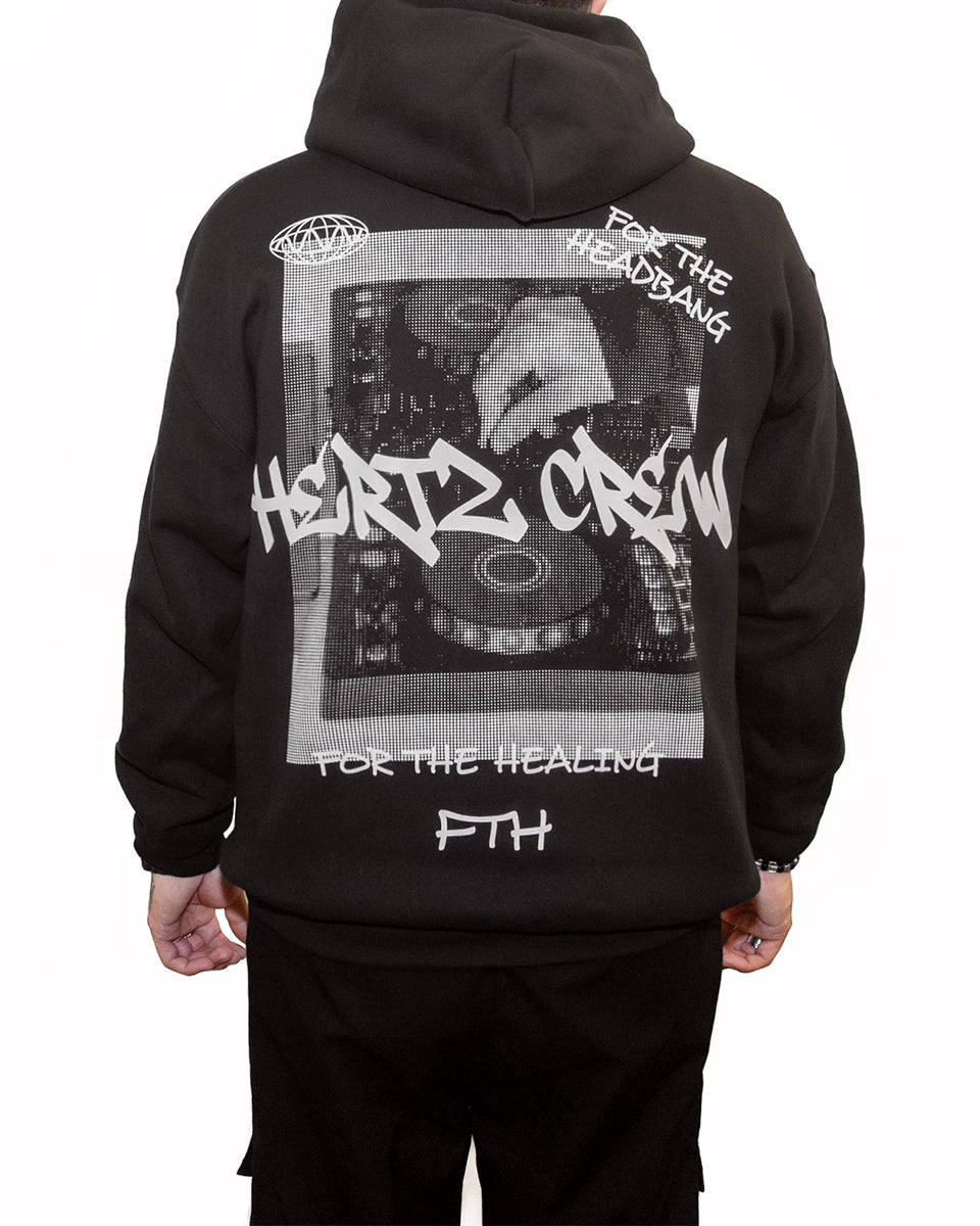 Person wearing a black hooded sweatshirt with a halftone print of hand playing dj controller. Includes hertz crew in graffiti font, handwritten text and logo on the back.