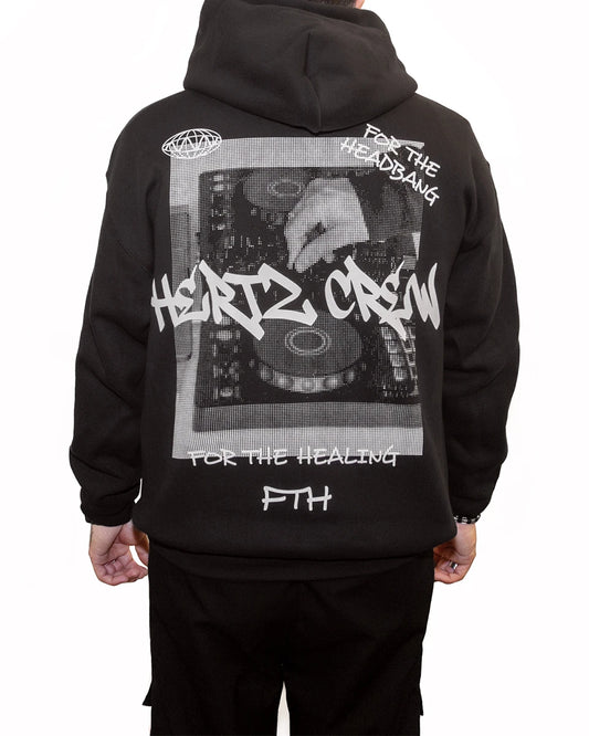 Person wearing a black hooded sweatshirt with a halftone print of hand playing dj controller. Includes hertz crew in graffiti font, handwritten text and logo on the back.