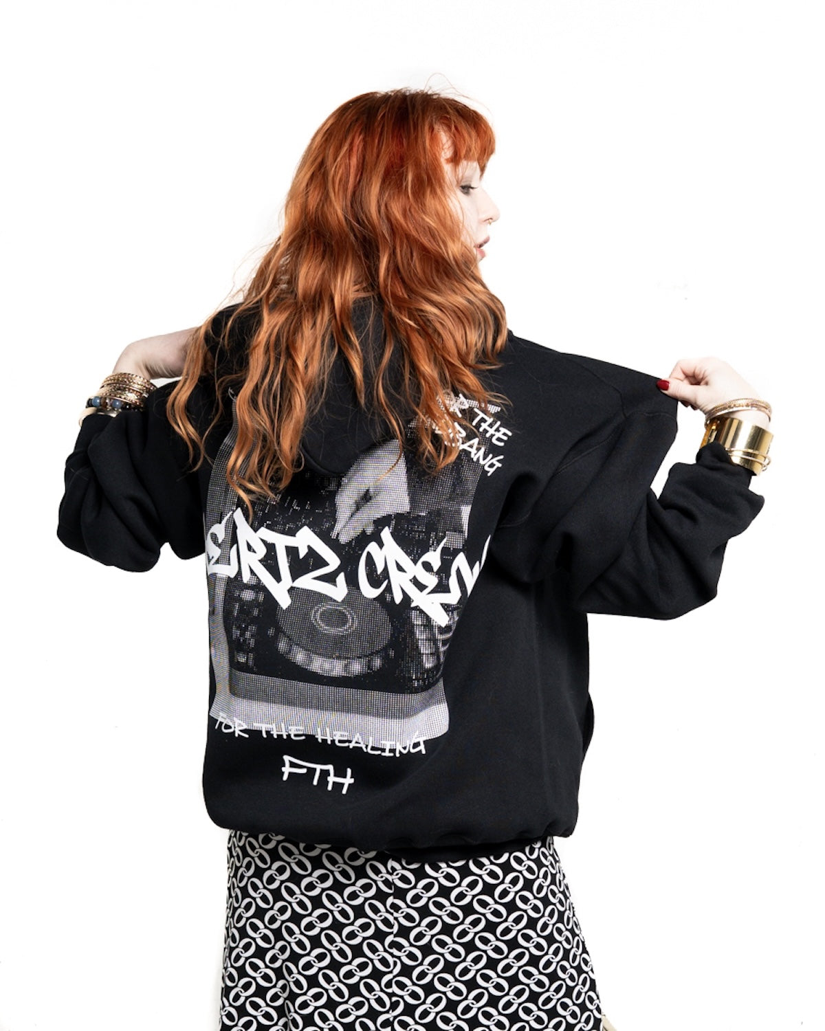 red headed woman wearing a black hooded sweatshirt with hertz crew in graffiti font with halftone of hand playing dj controller