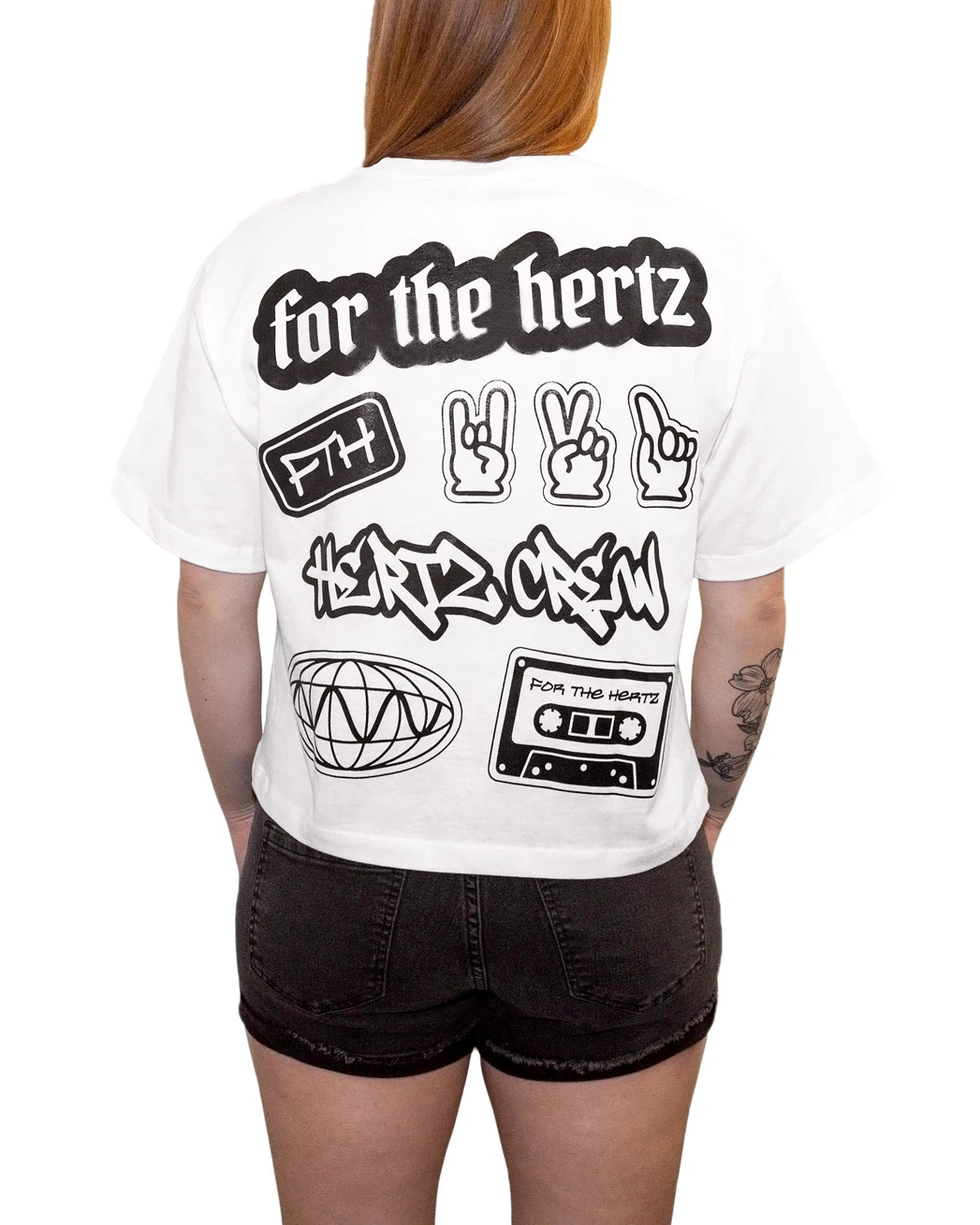 Red headed woman wearing white boxy crop t-shirt with text and graphic stickers on the back and black shorts